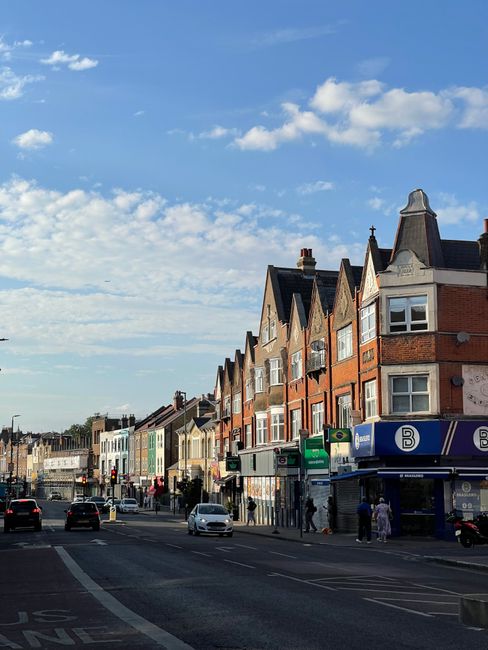 An aerial view of a small commercial building in Hither Green with a white facade and a teal awning, featuring a shopfront and flower displays outside. Several vehicles, including a black car, a green